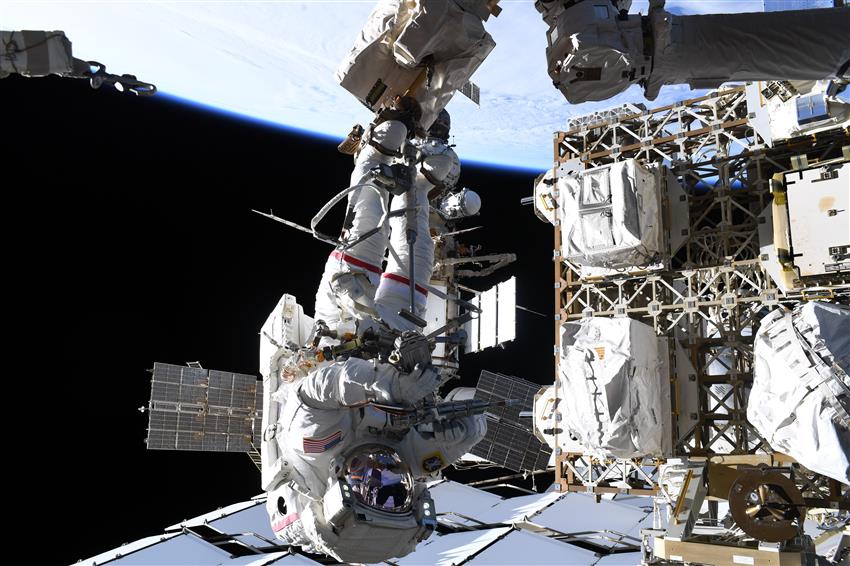 Anil travaille à l'extérieur de la Station, positionné sur le Canadarm2 et vêtu d'une combinaison spatiale.