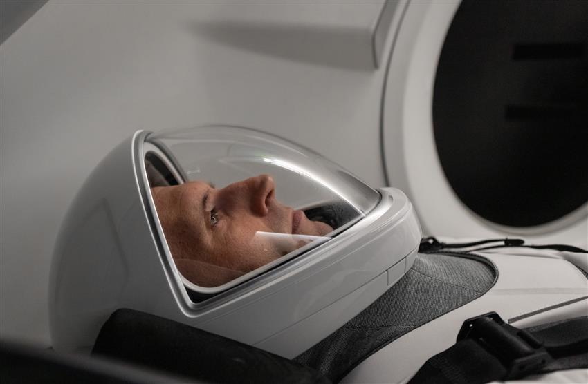Gros plan de Joshua portant un casque. Il se trouve dans le siège incliné d'une maquette de capsule Dragon.