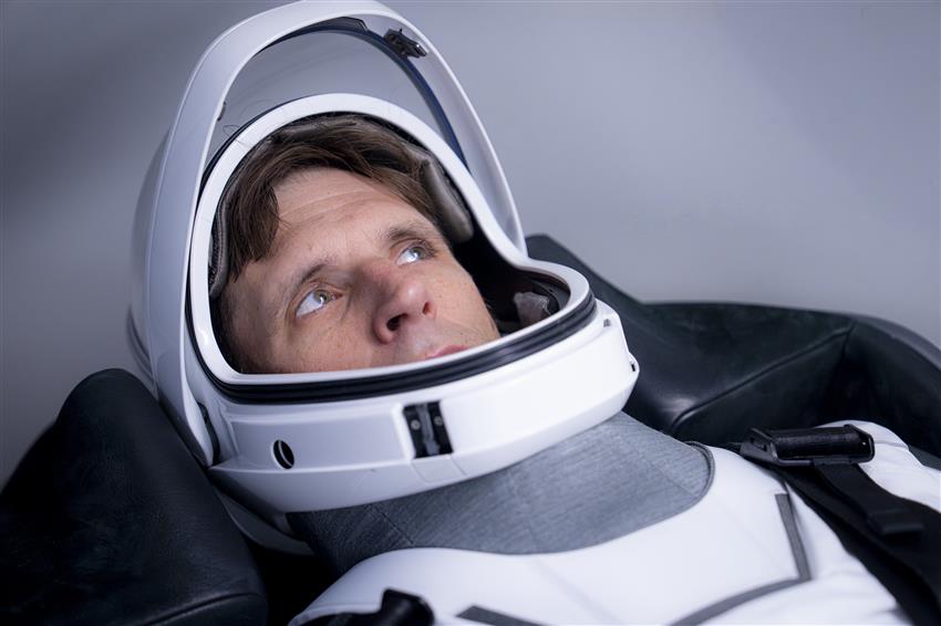 Gros plan de Joshua vêtu d'une combinaison spatiale de SpaceX dans le siège d'une maquette d'un vaisseau Dragon.