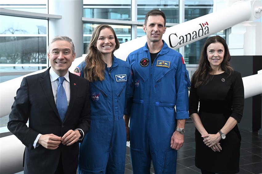 Four people pose for a picture. Two of them are in a blue flight suit.