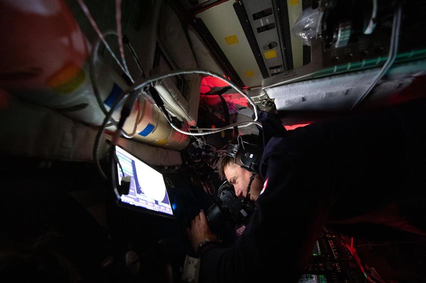 Dans la capsule Orion, Jeremy tient un appareil photo sur la vitre d'un hublot. 