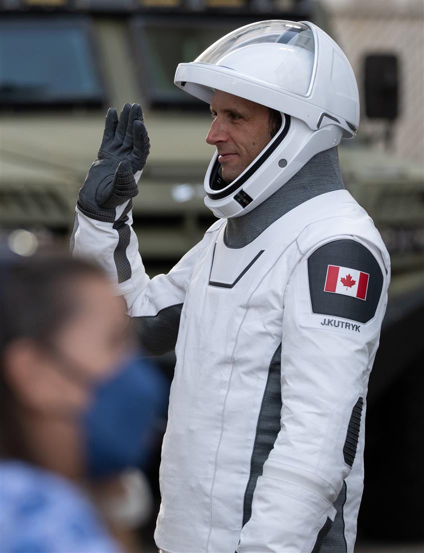 Joshua, wearing his flight suit, standing before the media and greeting the crowd with his right hand.