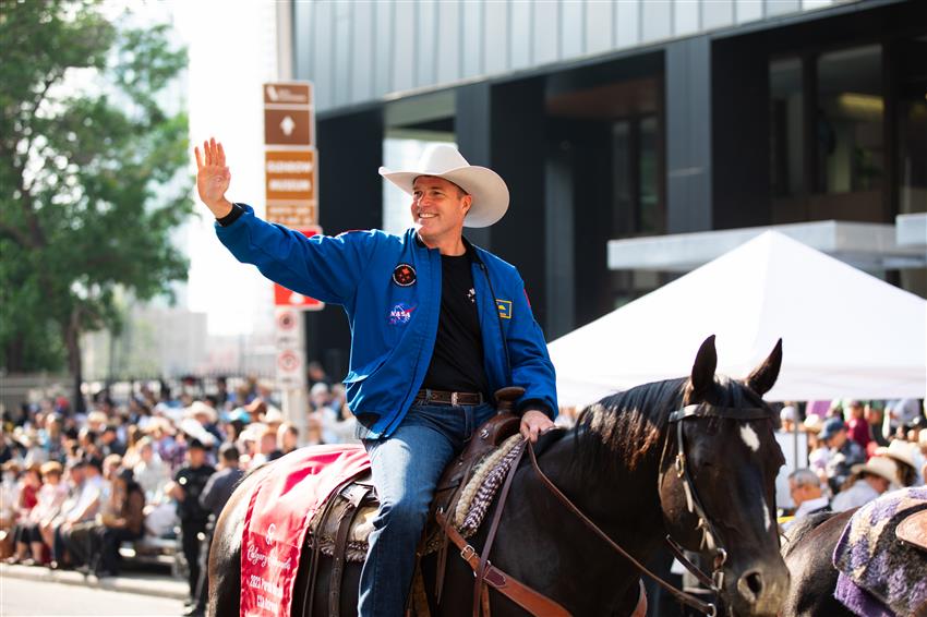 Jeremy Hansen waves to families gathered along a street as he rides a horse
