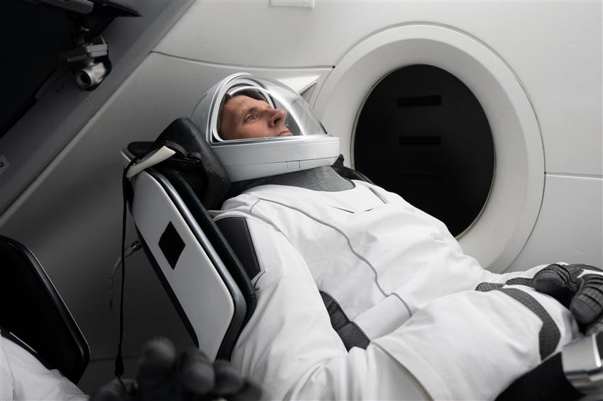 Joshua wears a space suit while reclining in a seat in a space capsule mock-up. 