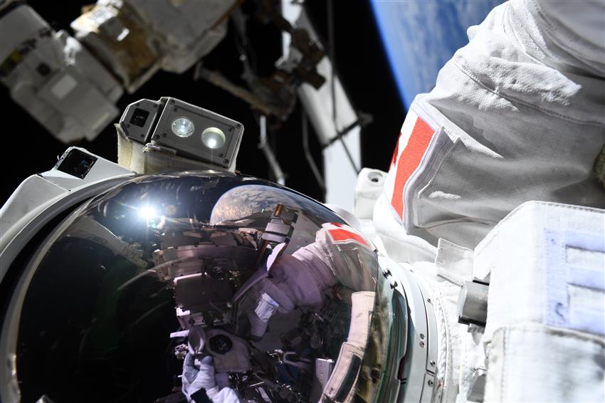 Joshua, vêtu d'une combinaison spatiale à l'extérieur de la Station, avec la Terre en arrière-plan.