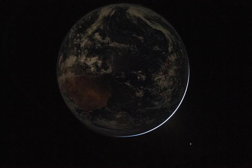 La Terre, plongée dans l'obscurité, avec un très mince croissant de lumière en bas à droite. 