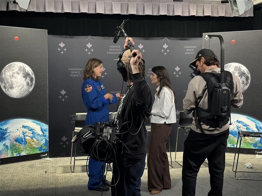Jenni speaks with Alexane. A man holds a microphone overhead while a cameraman films.