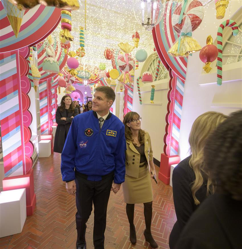 Jeremy and Catherine walk in a hallway adorned with candy-themed holiday decorations.
