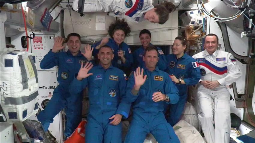 The astronauts from both crews gather in a semicircle inside the Station for the welcome photo.