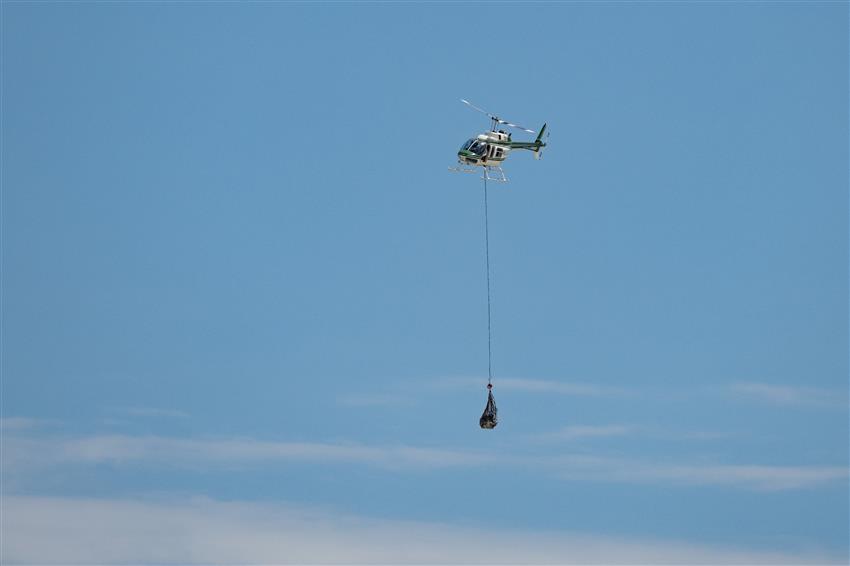 A helicopter transports a mock return capsule in a net hanging underneath it.