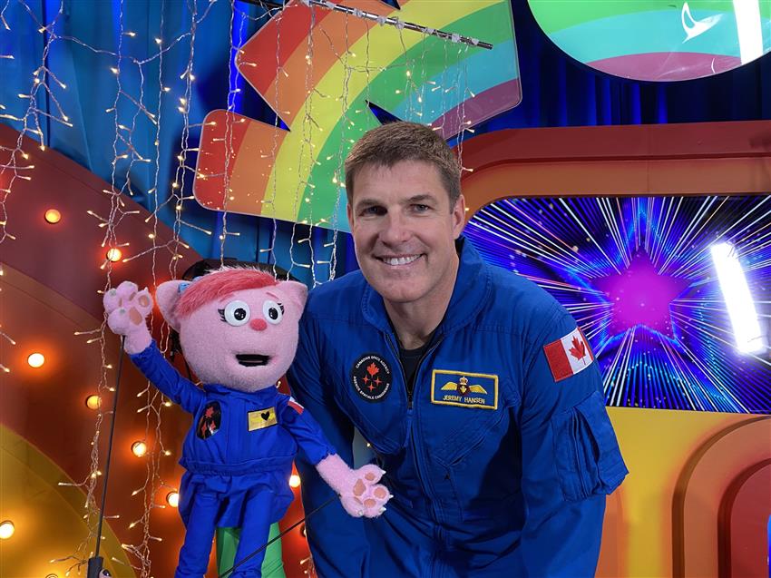 A man in a blue flight suit poses with a cat puppet wearing a matching flight suit.