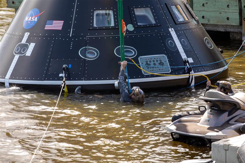 A recovery team member is seen floating in front of a training mock-up of Orion in a body of water