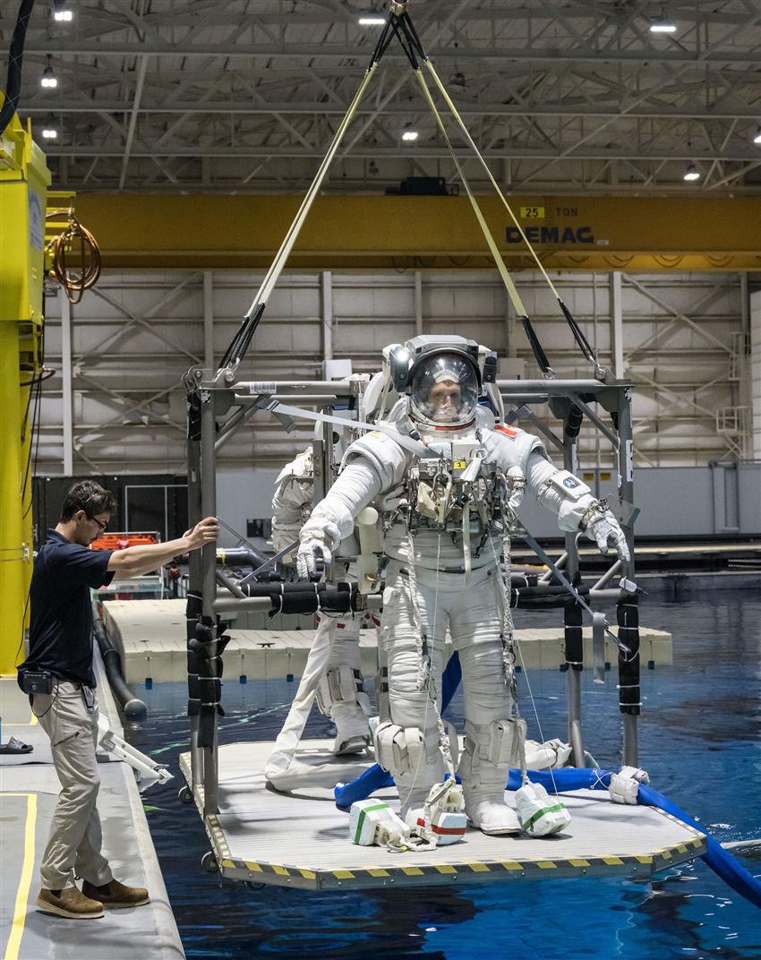 Joshua vêtu d'une combinaison spatiale, debout sur une plateforme au-dessus d'une piscine.