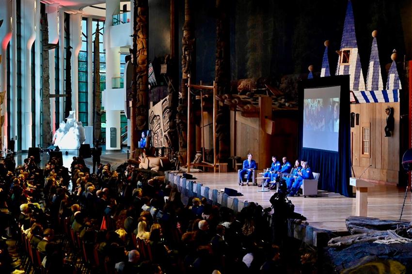 The five astronauts and Brian on stage in front of a large audience.