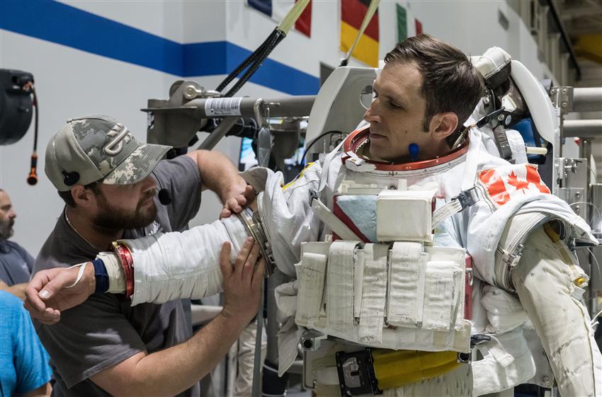 Un technicien installe un des bras d'une combinaison spatiale que porte Joshua.
