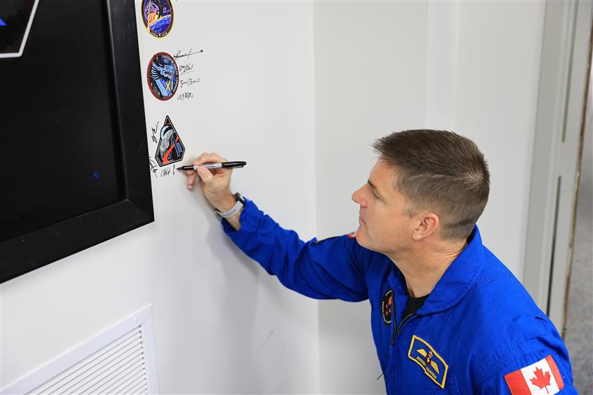 Jeremy appose sa signature sous un écusson posé sur un mur. 