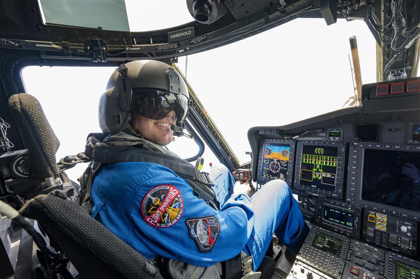 Jeremy in a cockpit, smiling, holding a joystick and wearing a helmet.