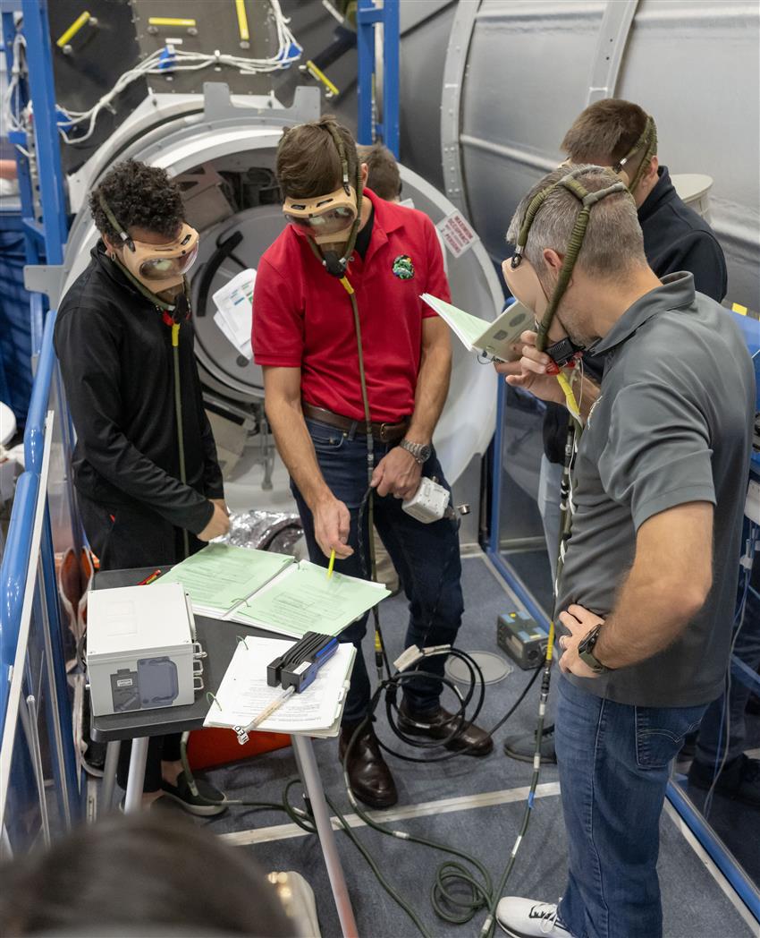 Jessica, Joshua, Andrey, and Luke wear protective breathing masks and consult a training manual. 