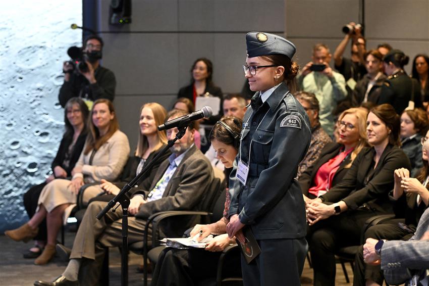 Close-up of the Air Cadet standing in front of a microphone in a crowded conference room.