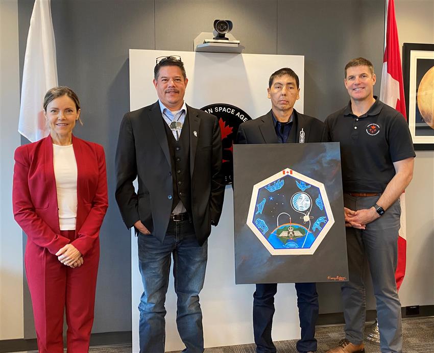 A woman and four men pose. The artist holds the painting of the mission patch.