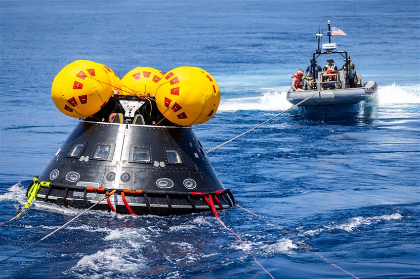 People aboard a boat tow a tear-shaped spacecraft.