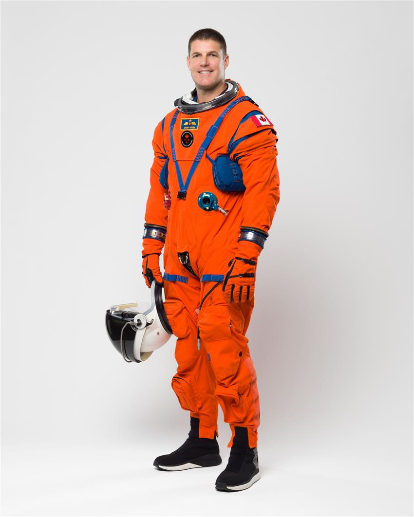 Plan en pied de Jeremy Hansen, un peu de profil, vêtu de sa combinaison de vol orange d'Artemis II